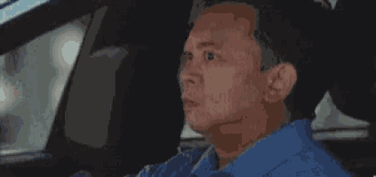 a man in a blue shirt is sitting in the driver 's seat of a car .