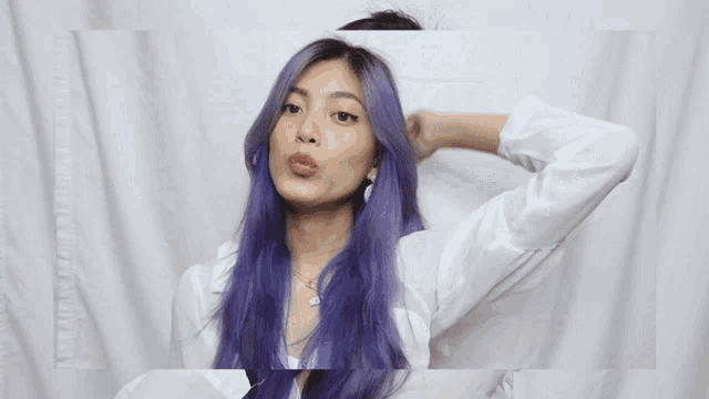 a woman with purple hair and a white shirt holds her hair