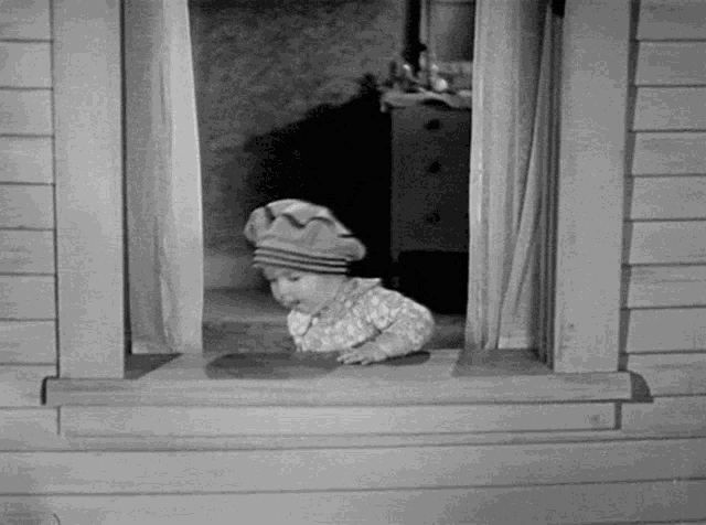 a black and white photo of a little girl looking out a window