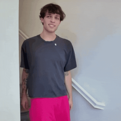 a man wearing a grey shirt and pink shorts is standing in front of a staircase