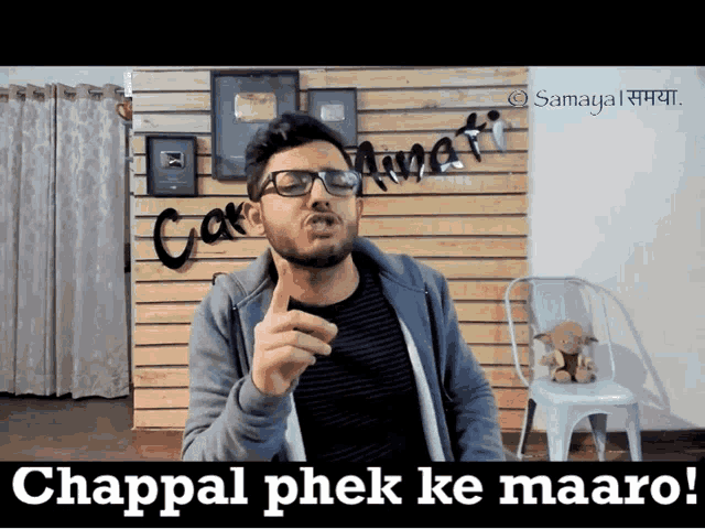 a man wearing glasses stands in front of a wooden wall with the words chappal phek ke maaro