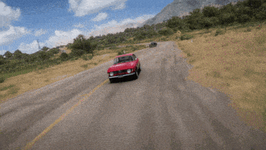 a red car is driving down a road with a mountain in the background