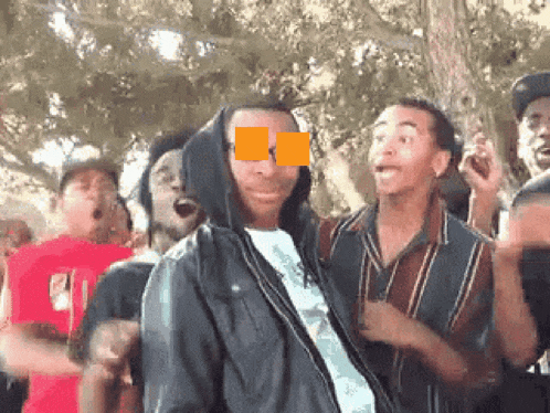 a group of young men are dancing in a park with a man wearing a hoodie covering his eyes