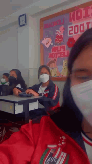 a girl wearing a face mask sits at a desk in front of a bulletin board that says " 2001 "