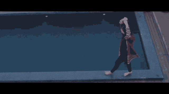 a woman in a red and black striped sweater is walking along the edge of a swimming pool