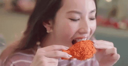 a woman is eating a fried chicken wing with her mouth open .