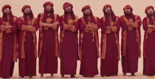 a group of people in long red dresses are dancing in the desert .