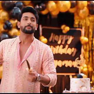 a man in a pink shirt is standing in front of a cake and balloons .
