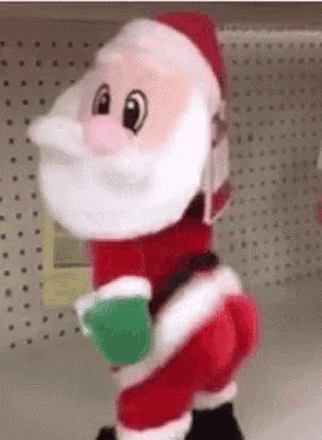a stuffed santa claus is standing on a shelf holding a green cup .