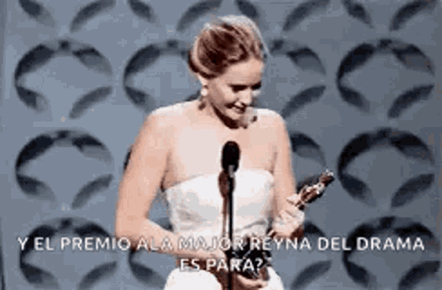 a woman in a white dress is holding a trophy in front of a microphone at an awards ceremony .