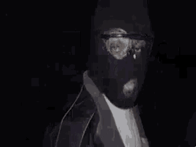 a man wearing a black ski mask and sunglasses is standing in the dark .
