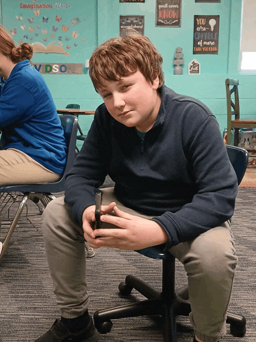 a boy sits in a chair in front of a wall with a sign that says imagination