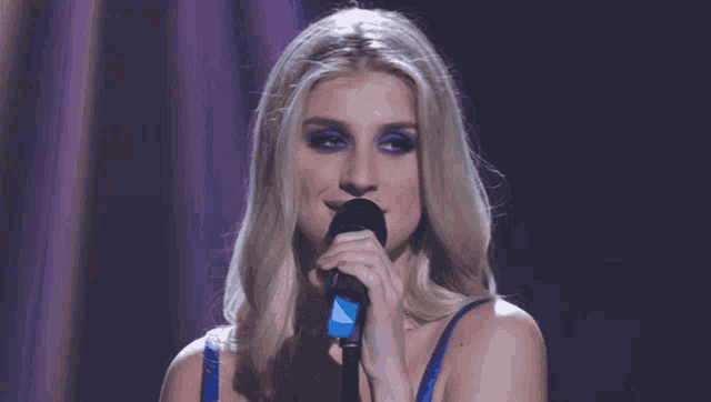 a blonde woman singing into a microphone with blue eyeshadow