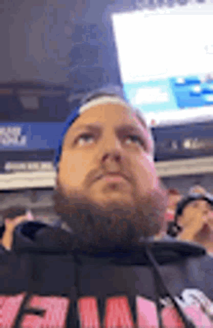 a man with a beard and a headband is sitting in front of a screen .
