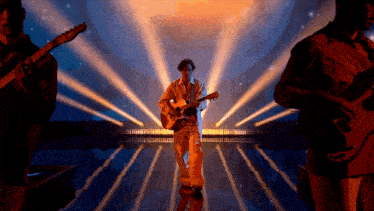 a man playing an acoustic guitar on a stage with other men playing guitars