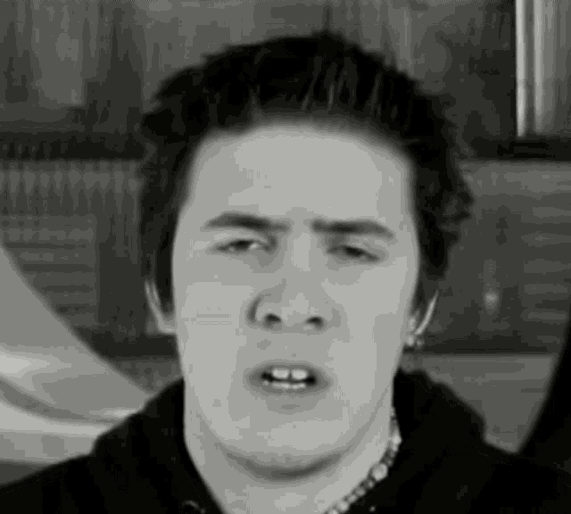 a black and white photo of a young man with a necklace around his neck making a funny face .