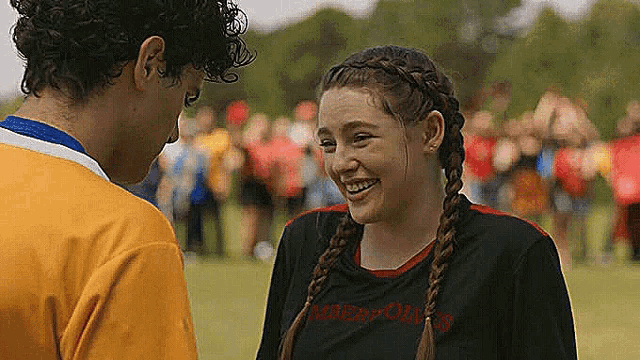 a boy and a girl are laughing together on a field . the girl is wearing a braided headband .