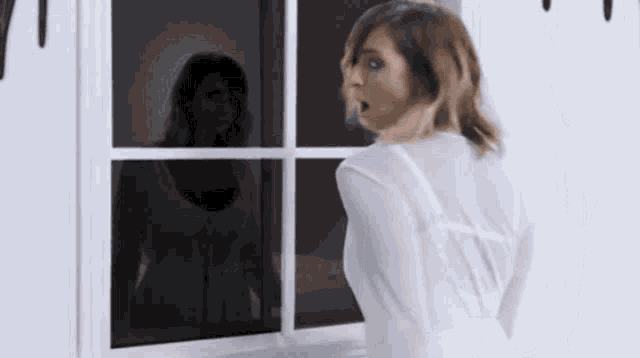 a woman in a white robe is looking out a window