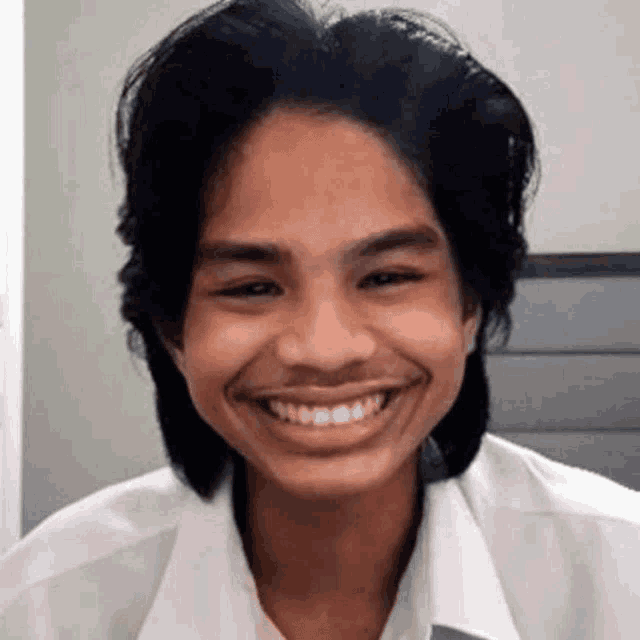 a young man with long hair and a white shirt is smiling .