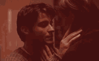 a man and a woman are kissing in a dark room and the woman is touching the man 's neck .
