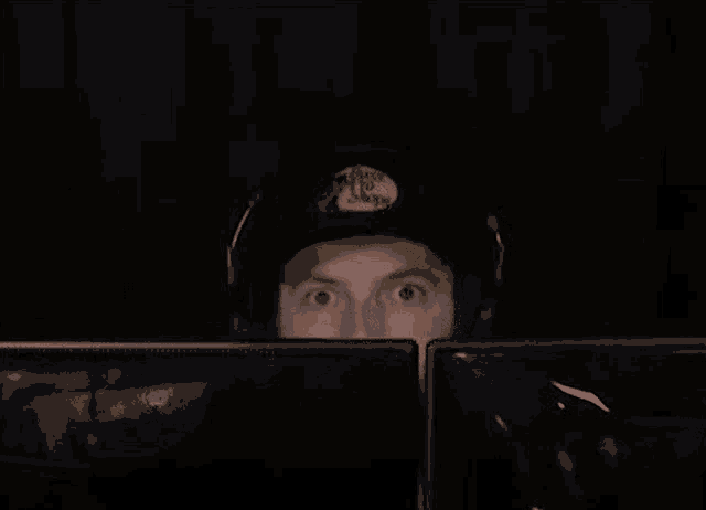 a man wearing headphones and a hat is looking at two computer monitors in a dark room .