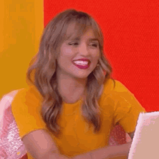 a woman in a yellow shirt is smiling while looking at a laptop .