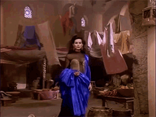 a woman in a blue dress is standing in a room with clothes hanging on a clothes line .