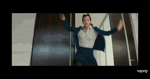 a woman in a suit and skirt is jumping in the air while holding a cell phone .