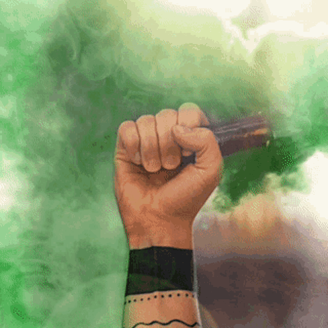a person with a tattoo on their wrist is holding a green smoke bomb in their fist