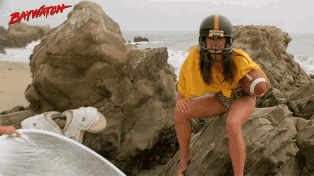 a woman wearing a football helmet is holding a football in front of a baywatch logo