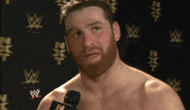 a man with a beard is talking into a microphone in front of a wall with nxt logos