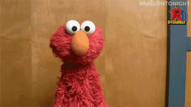 elmo from sesame street is standing in front of a wooden door and looking at the camera .