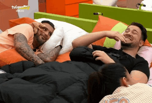 two men are laying on a bed and one of them is making a face with his hand