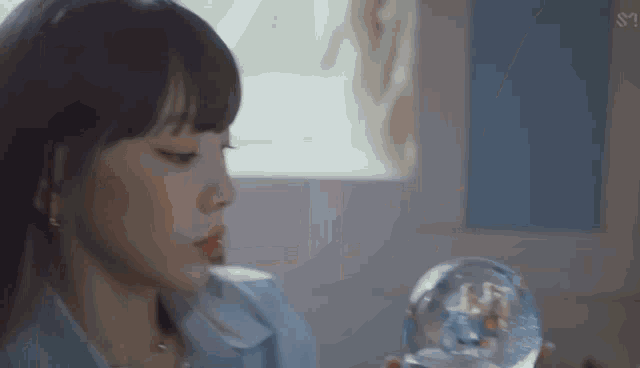 a close up of a woman holding a snow globe in front of a window .