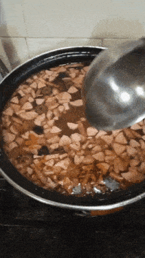 a ladle is pouring liquid into a pot filled with chopped meat