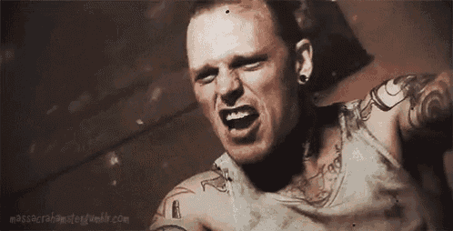 a man with a lot of tattoos on his arms and chest is screaming in a dark room .