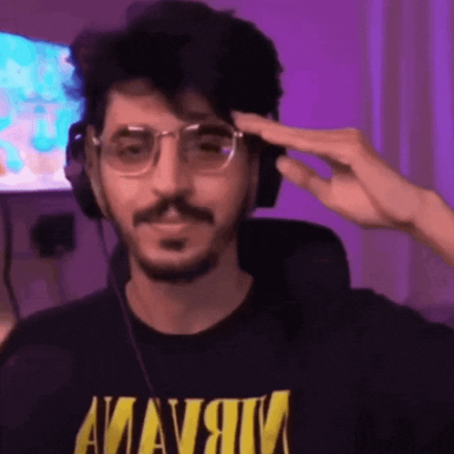 a man wearing glasses and headphones is saluting while wearing a black shirt with the word nirvana on it .