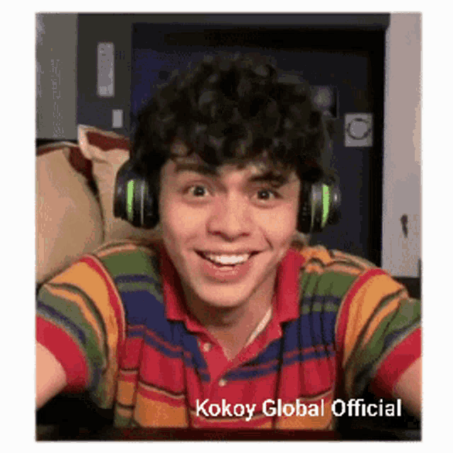 a young man wearing headphones and a striped shirt is smiling for the camera .