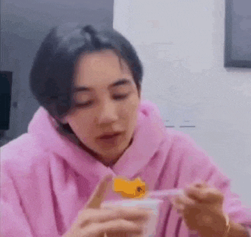 a young man in a pink hoodie is eating a yogurt with a spoon .