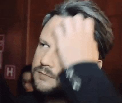 a man with a beard is holding his hand to his forehead and making a funny face .