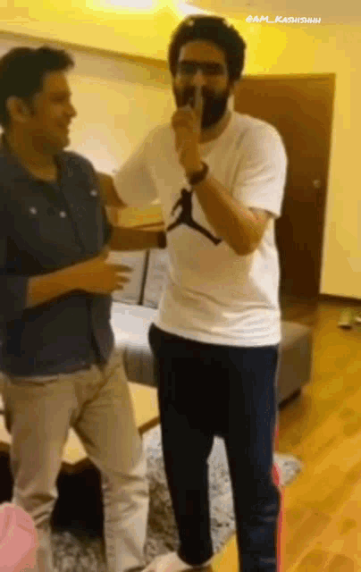 two men are standing in a living room and one is wearing a white shirt that says jordan