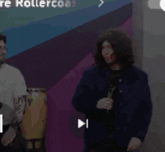 a man wearing a wig and a blue jacket is standing in front of a mirror .