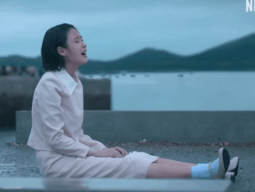 a woman in a pink dress sits on the ground with a n on the bottom right