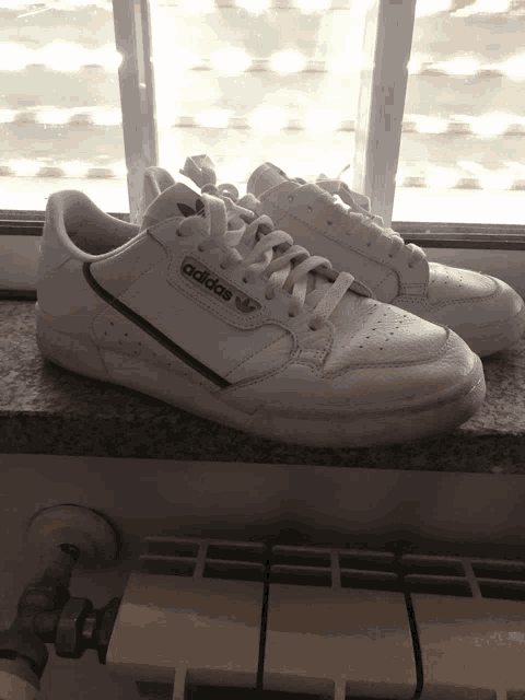 a pair of white adidas sneakers are sitting on a window sill
