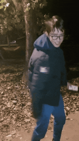 a young boy wearing glasses and a black jacket is standing in a park at night