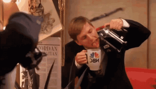 a man in a suit is drinking from a mug that says nbc on it