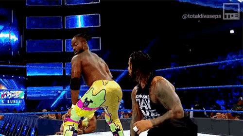 two men are wrestling in a wrestling ring . one of the men is wearing a tank top that says `` own style '' .