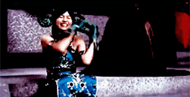 a woman in a blue dress is holding a snake in her hand