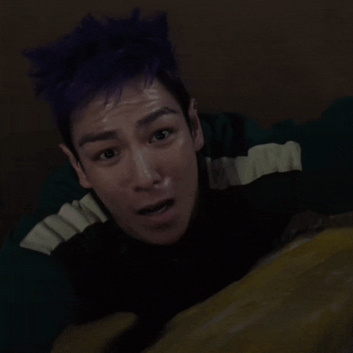 a man with purple hair is laying on his back with his mouth open