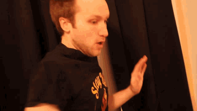 a man wearing a black shirt with the word now on it making a funny face